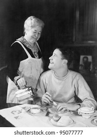 Mother pouring coffee for teenage son
