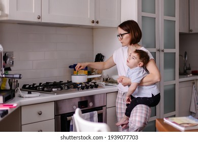 Mother Prepares Breakfast In The Kitchen With Her Disabled Child. A Kid With Cerebral Palsy In Her Mother's Arms. Housewife In Her Daily Routine. Tired Mom. Lifestyle Real Life