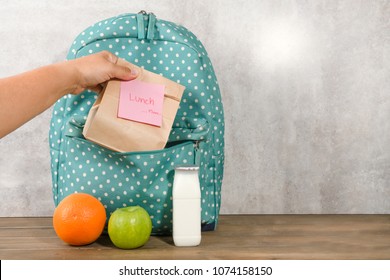 Mother preparing for her children lunch box with sandwich in paperbag orange apple and milk on wooden background. Back to school with lunch box concept. - Powered by Shutterstock