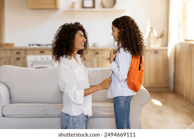 Mother preparing schoolgirl daughter for first school day after holidays, talking to girl at home interior, side view. Mother and child bond concept - Powered by Shutterstock