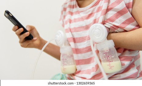 Mother pumping milk to bottles by Automatic breast pump machine while play social media, chat, and shopping online from smartphone with copy space for text.