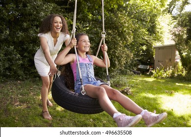 Mother Pushing Daughter On Tire Swing In Garden - Powered by Shutterstock