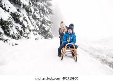 Mother Pushing Son On Sledge. Foggy White Winter Nature.