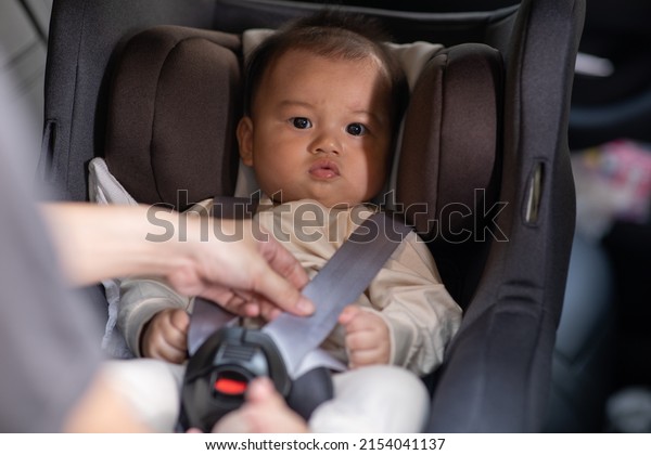 Mother put\
cute baby to car seat and secure with safety belts. Asian infant\
baby sit in baby seat and looking around in car.mom buckling her\
son to car seat.Baby safety on car\
concept