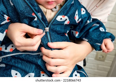 Mother puts a blue overalls on the toddler baby sitting in the home hallway. Woman mom dressing warm clothes coverall on child for winter walk in cold weather. Kid aged one year and three months - Powered by Shutterstock