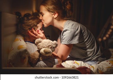  mother puts her daughter to bed and kisses her in the evening