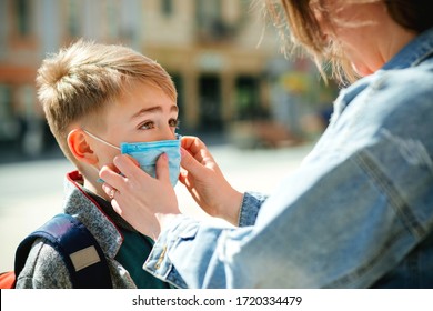 Mother puts a safety mask on her son's face. Schoolboy is ready go to school. Cute boy with a backpack outdoors. Back to school concept. Medical mask to prevent coronavirus. Coronavirus quarantine - Powered by Shutterstock