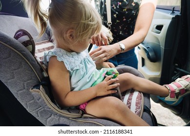 Mother putting baby girl into the car seat. Children care and safety on roads
