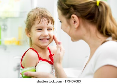 mother putting cream on her daughter's face in bathroom - Shutterstock ID 173409083