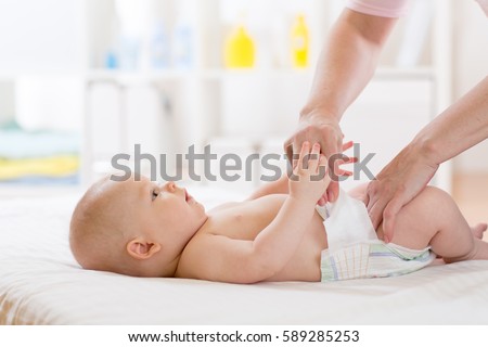 Mother putting diaper on her happy baby in nursery