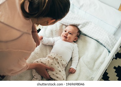 Mother Putting Her Newborn Baby To Sleep At The Crib.
High Angle View Of Young Mom Bending Forward Over A Crib To Check Her Cute Baby Who Is Looking At His Mum And Smiling