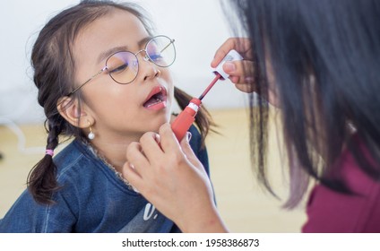 Mother Putting Lipstick On Her Daughter On Blurry Background. Mom Dresses Up And Makes Make-up Her Daughter. Selective Focus.