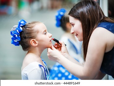 Mother Putting Lipstick On Her Daughter On Mirror Background. Woman Helping Little Gir To Use Lipstick Before A Dance Performance. Mom Makes Make-up Her Daughter. Selective Focus.