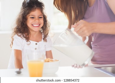 Mother Putting Milk In The Cereal Of His Daughter In Kitchen