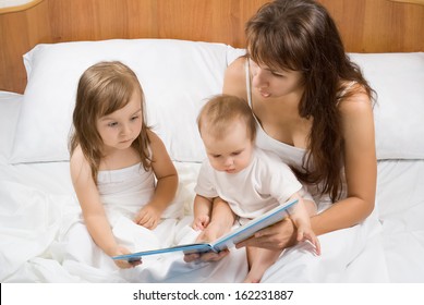 Mother Reading Bed Time Story Book To Children In Bed