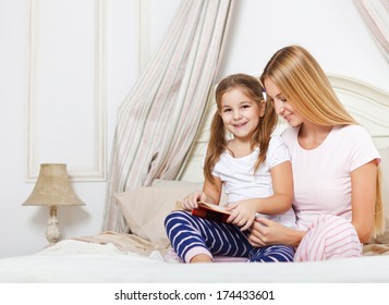 Mother Reading Bed Time Story Book To Her Daughter In Bed