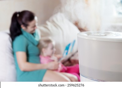 Mother reading book to her daughter on the blured background of humidifier