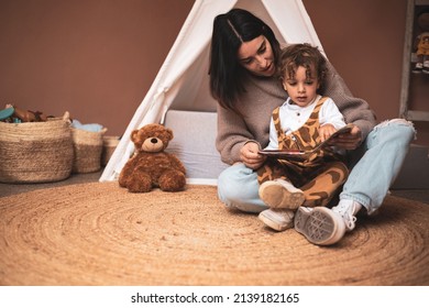 a mother reading a book to her little son in the bedroom before going to sleep. caucasian mom telling stories sitting on the floor.