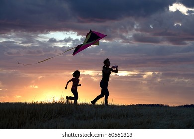 A mother runs to fly a kite with her daughter behind her.
