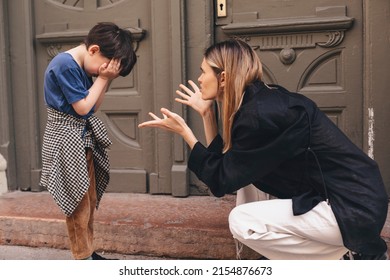 Mother scolds her son on the street. A child cries, a woman shakes her finger because of the boy bad behavior, while walking to home. Rule of conduct. Woman sitting, boy cover his face and cry. - Shutterstock ID 2154876673