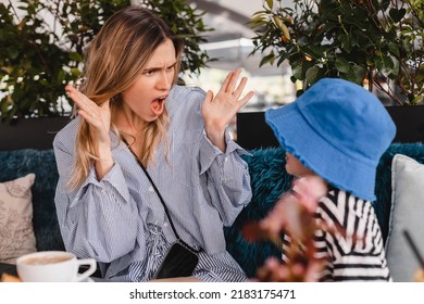 Mother Scolds Her Son Sitting In Restaurant. A Child Cries, A Woman Spread Her Hands Because Of The Boy Bad Behavior. Rule Of Conduct. Woman Sitting, Boy Look Gloomy, Pouts Lips And Cry. Rest In Cafe.