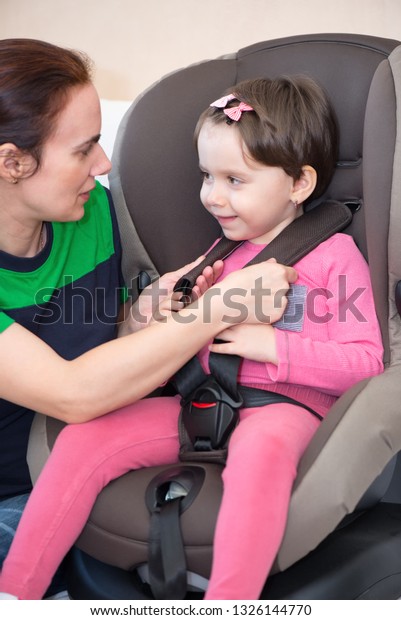 Mother securing daughter in the car seat, isolated\
with clipping path