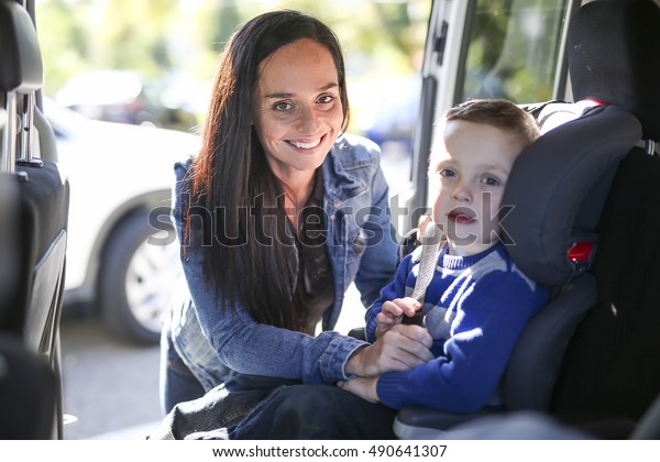 A\
Mother securing her boy in the car seat in her\
car