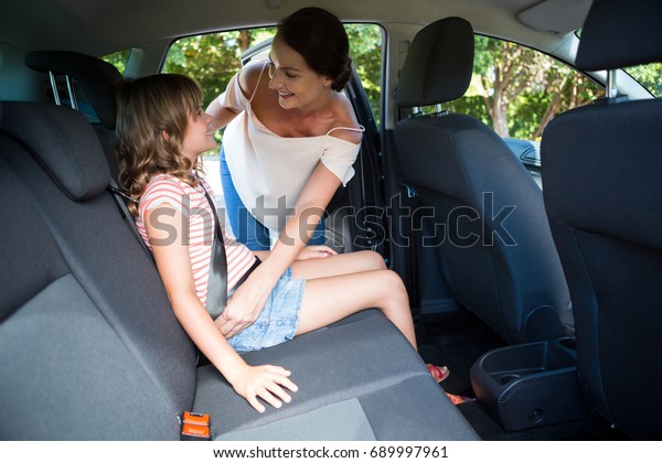 Mother\
securing her daughter with seat belt in a\
car
