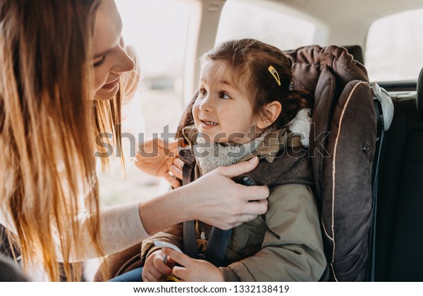Mother securing her toddler daughter in the coat\
buckled into her baby car\
seat