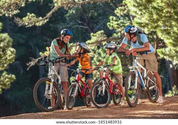 Mother securing the strap of her\
daughter\'s helmet and the family is ready for a cycling\
adventure