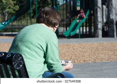 A Mother Seems More Interested In Looking At Her Phone Than Paying Attention To Her Child.