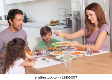 Mother serving vegetables to daughter at dinner in kitchen