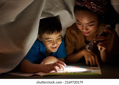 Mother Shining Flashlight On Book Page When Son Reading Scary Story