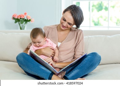 Mother Showing Picture Book To Son While Siting On Sofa At Home