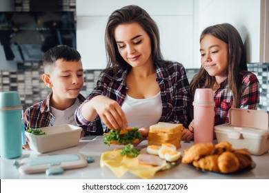 Mother Sit In The Kitchen Making Breakfast For Her Children In The Morning And A Snack With Lunch Box For School.