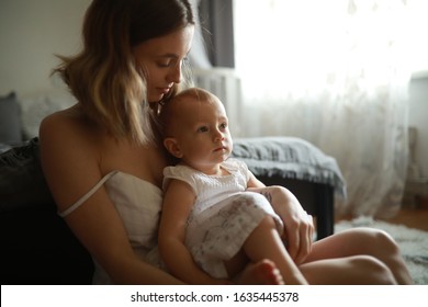 Mother sits with her little daughter at the room on the sofa.