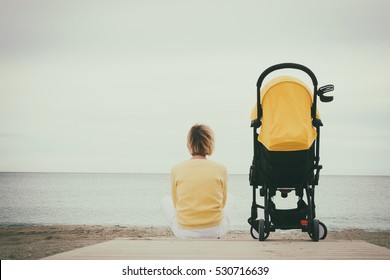 Mother sitting alone next baby stroller on beach by the sea. Cloudy sky with copy space - Powered by Shutterstock