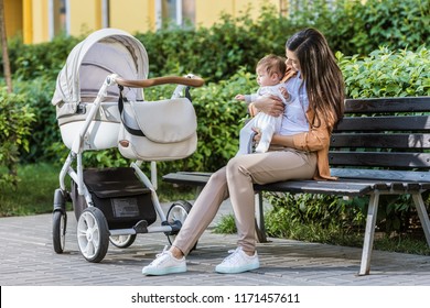 mother sitting with baby on bench near stroller in park