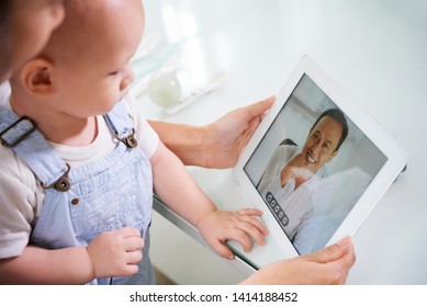 Mother sitting with baby on laps and video calling her husband via tablet computer - Powered by Shutterstock