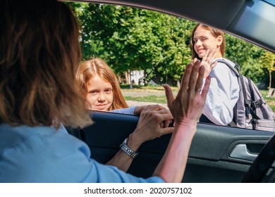 Mother Sitting Inside The Car And Gesturing With Hand Goodbye And Leaving Her Daughters In School Uniform At School.