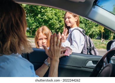 Mother Sitting Inside The Car And Gesturing With Hand Goodbye And Leaving Her Daughters In School Uniform At School.