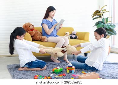 Mother Sitting On Sofa And Surfing Internet, Mom Online Working By Using Tablet Or Social Addiction While Her Kid Daughter Snatching Toys, Mom Not Paying Attention To Children, Sister Quarrel Fight.