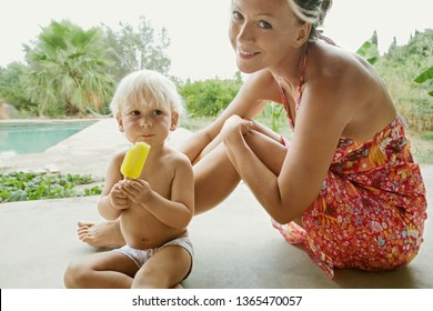 Mother Sitting With Son Child By Holiday Villa Swimming Pool And Garden, Boy Eating Ice Cream, Smiling Together Outdoors. Family In Hotel Pool Enjoying Summer Vacation, Leisure Recreation Lifestyle.