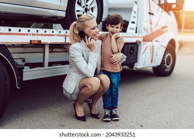 An mother with a small child wait for a tow truck to take away their broken car.