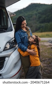 Mother With Small Daughter Hugging By Car Outdoors In Campsite At Dusk, Caravan Family Holiday Trip.