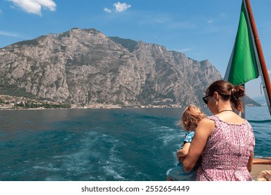 Mother with small toddler on ferry tour looking at lakeside town Limone Sul Garda, Lombardy, Northern Italy. Surrounded by mountain peaks of Garda Hills. Summer lakeside atmosphere. Italian flag - Powered by Shutterstock