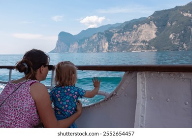 Mother with small toddler on ferry tour looking at lakeside town Limone Sul Garda, Lombardy, Northern Italy. Surrounded by mountain peaks of Garda Hills. Summer lakeside atmosphere. Italian flag - Powered by Shutterstock