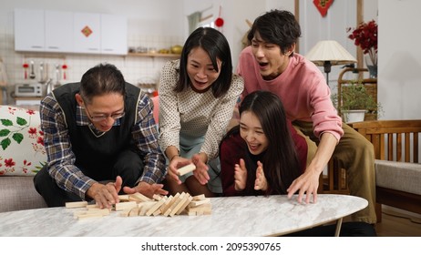 mother smiling with embarrassment as she makes the tumbling tower fall. happy chinese family of four enjoying toy wood blocks game together at home during spring festival chinese new year