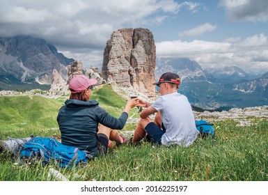 Mother and son backpackers have a picnic on a green mountain hill with the picturesque Dolomite Alps Cinque Torri formation, Nothern Italy. Family values, active people and mountains concept.
