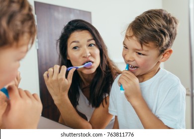 Mother and son brushing teeth in bathroom. Woman with her son brushing teeth together and looking in mirror. - Powered by Shutterstock